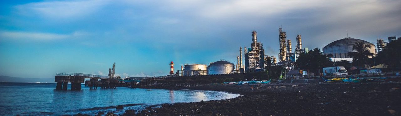 Industrial buildings by the sea under a dramatic cloudy sky.