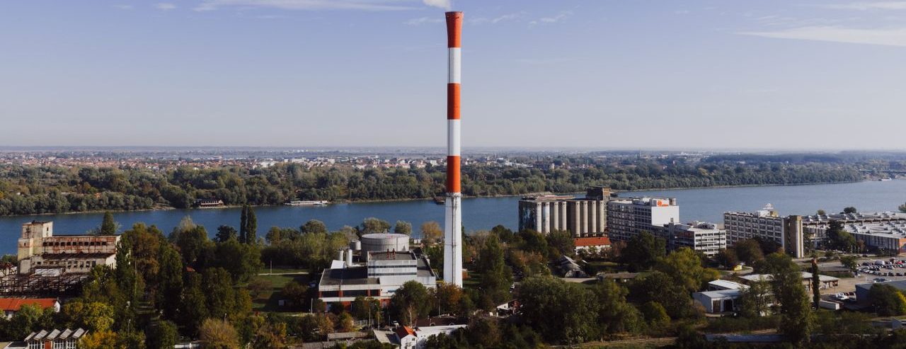 Aerial view of Belgrade's industrial area with smokestack and river on a clear day.