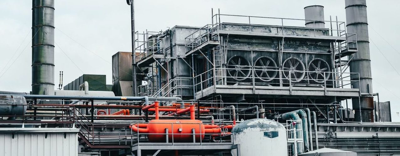 Industrial factory with metal pipes and special equipment surrounded with fences located against cloudy sky on street with power lines in town